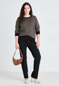 Un pantalon noir associé à un pull à motifs présentant des formes géométriques en or et noir. Un sac à main marron et des talons compensés crème complètent le look.