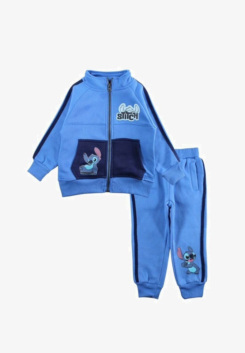 Survêtement en polaire bleu comprenant une veste zippée et un pantalon assorti. La veste présente des accents bleu marine et un motif du personnage Stitch sur les poches.