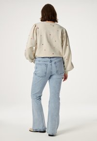 Lichtbeige sweatshirt met bloemenborduursel, gecombineerd met lichtblauwe flared jeans. De outfit heeft een ontspannen pasvorm en een zachte textuur.