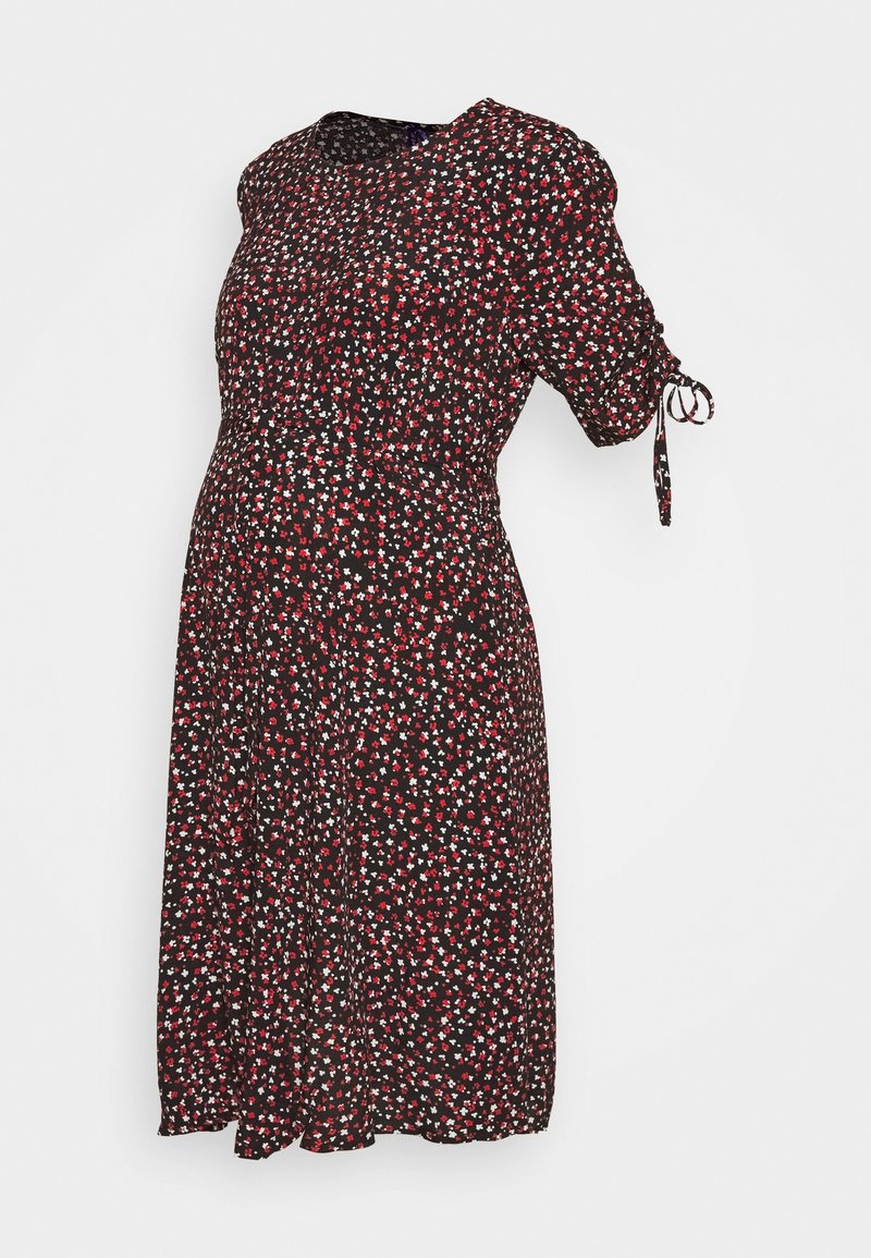 Robe de maternité noire avec un petit motif floral rouge et blanc, encolure ronde et manches courtes avec un détail de noeud.