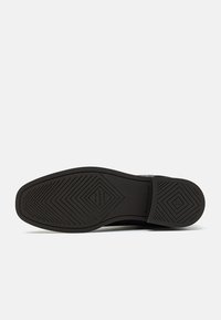 Semelle d'une chaussure de ville noire avec un motif de bande de roulement géométrique, nom de la marque "GANT", taille 37, et inscription "Fabriqué en Italie".