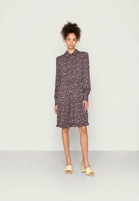 Vestido floral em azul marinho escuro com padrões em rosa e branco, mangas longas, colarinho e barra com volantes. Acompanhar com sandálias de salto bloco amarelas.