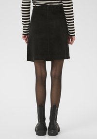 Čierna manšestrová sukňa s priliehavým pásom, dizajn dĺžky po kolená a jemnými vertikálnymi ryhami; skombinovaná s čiernymi členkovými čižmami.