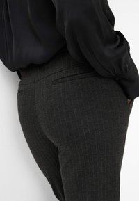 Grijze gestreepte broek met een tailored fit, voorzien van een gladde textuur, achterzakken en een middelhoge tailleband. Gecombineerd met een zwarte blouse.