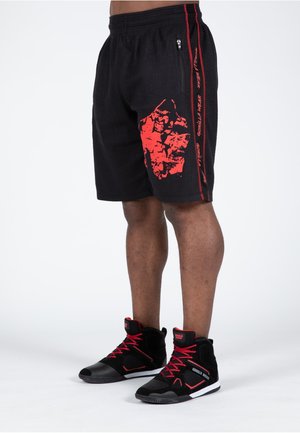 Schwarze Sportshorts mit strukturierter Oberfläche, die mit einem roten Grafikdruck und seitlichen Streifen versehen sind. Kombiniert mit schwarzen High-Top-Sneakers mit roten Akzenten.