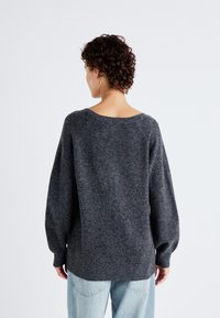 Maglione grigio oversize in lana a maglia con scollatura ampia e maniche lunghe e larghe. Texture morbida, con orlo a coste e design semplice.