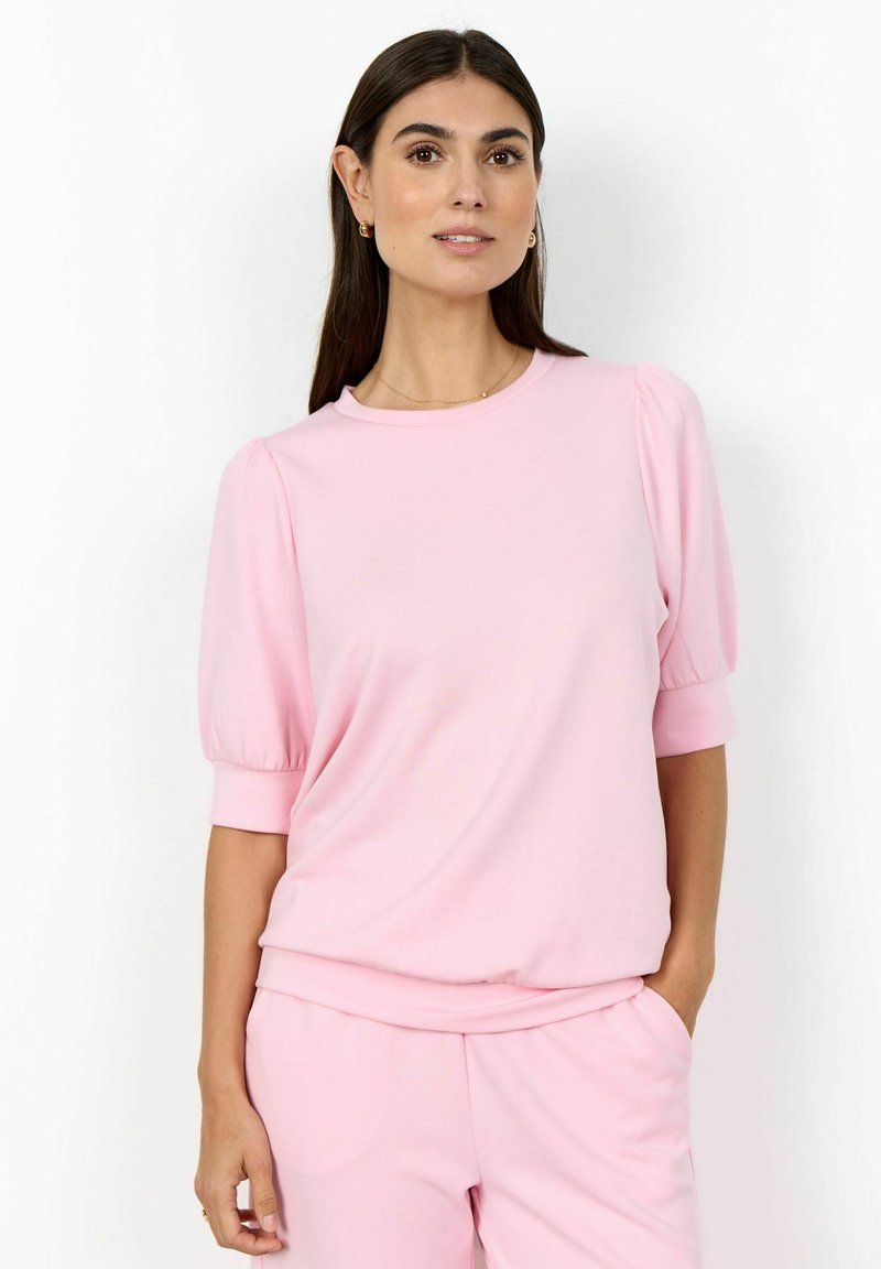 Ružové tričko s krátkym rukávom z mäkkej látky, s okrúhlym výstrihom a nafúknutými rukávmi. V kombinácii s ružovými nohavicami v rovnakom odtieni pre jednotný vzhľad.
