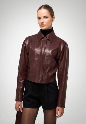 Bordeaux leren cropped jack met een puntige kraag, voornaden en een getailleerde pasvorm. Zachte textuur, lange mouwen en minimale hardware.