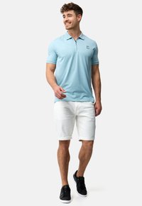 Lyseblå polo shirt med korte ærmer og lynlåskrave, parret med hvide rullede shorts og sorte sneakers. Casual design og pasform.