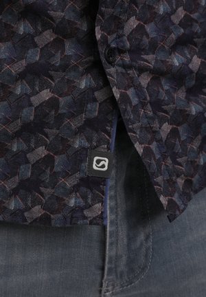 Dolgi rokav srajca iz temnega blaga z geometričnim vzorcem v odtenkih modre, sive in z rjavimi poudarki. Vključuje črno oznako z logotipom.