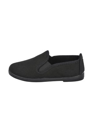 Zapato negro de lona tipo slip-on con panel elástico lateral y suela plana de goma, mostrado de perfil sobre un fondo blanco.