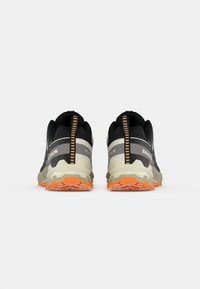 Pair of black and gray trail running shoes with orange soles, viewed from the back on a white background.