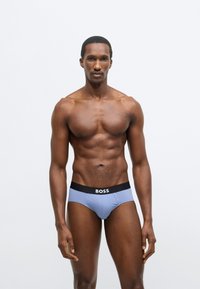 Chiloți pentru bărbați din țesătură albastru deschis, cu talie neagră pe care este inscripționat numele brandului "BOSS" în alb. Textură netedă, croială ajustată.