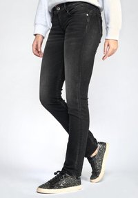 Jeans skinny en denim noir avec une texture lisse, dotés d'une taille mi-haute et d'un design classique à cinq poches. Associés à des baskets noires pailletées.