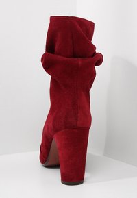 Botín de ante rojo hasta el tobillo con un diseño de puño doblado, tacón alto de bloque y textura suave. La vista trasera muestra los detalles de la parte superior y el tacón.