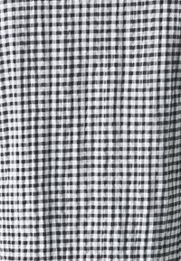 Tissu vichy noir et blanc avec un tissage texturé, présentant un motif en grille régulière de carrés. Le fond est délicatement plissé.