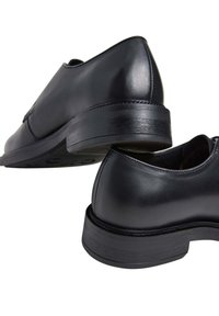 Scarpe in pelle nera con una finitura liscia, punta rotonda e tacco impilato; presentano un sottile dettaglio di cucitura sulla tomaia.