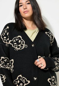 Mustakardigaani, jossa on beige leopardi kuviot, syvä V-pääntie ja yksi napin sulku. Pehmeä neulottu rakenne ja pitkät hihat.