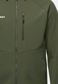 Giacca softshell verde oliva con tasca sul petto con zip, texture liscia e zip nere a contrasto. Design senza cuciture con accenti minimi.