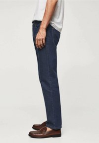 Vaqueros de mezclilla en azul oscuro con un diseño de pierna recta, combinados con mocasines marrones. Cuenta con bolsillos y una cintura sin costuras.