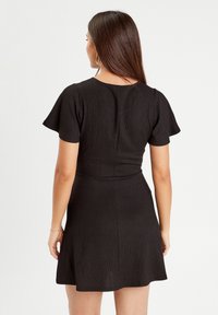 Robe noire à manches courtes en tissu texturé ; corsage cintré et jupe évasée, avec un col rond et une fermeture éclair à l'arrière.