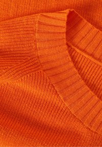 Primo piano di un maglione arancione lavorato a maglia che mostra il colletto a coste e le diverse trame del tessuto.