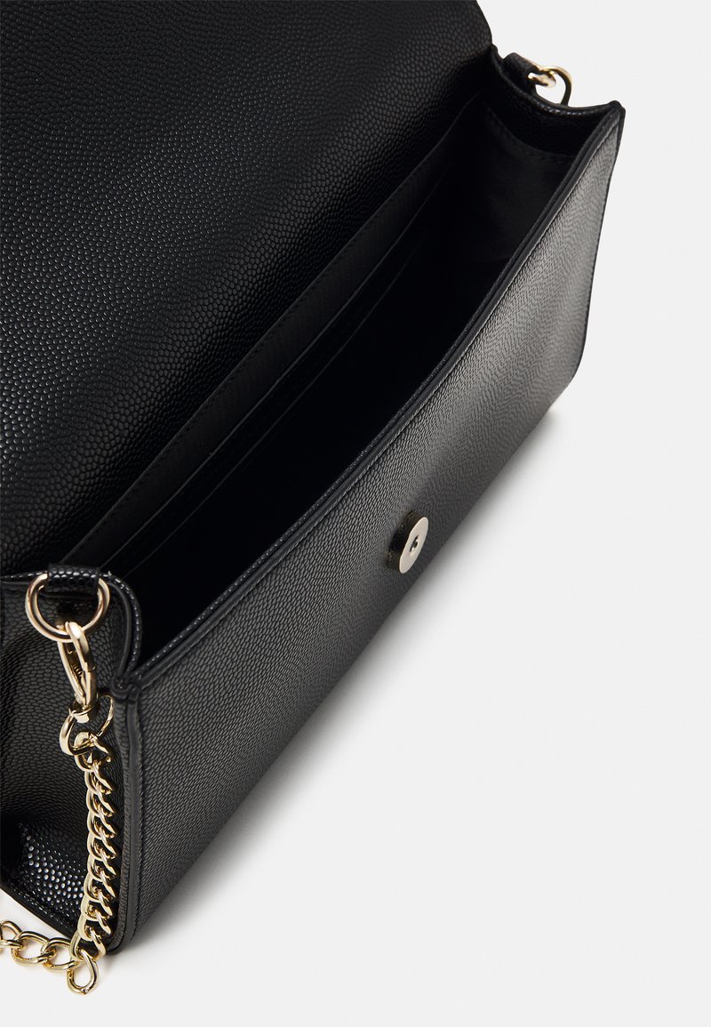 Sac à main en cuir noir avec une finition texturée, accent en chaîne dorée et fermeture magnétique. L'intérieur comprend plusieurs compartiments pour l'organisation.