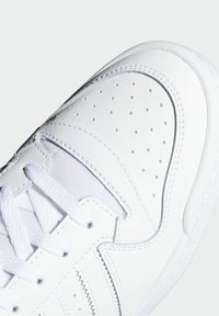 White athletic shoe with a smooth leather upper, perforated toe box, white laces, and contrasting stitching. Rounded toe and textured sole.