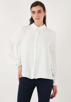 White long-sleeve blouse with a button-down front, collar, and gathered elastic cuffs. Smooth fabric and flowing design.