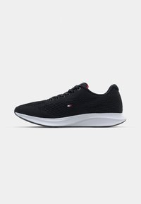 Chaussures de sport noires avec un dessus en maille, design à lacets, semelle blanche et détail de logo subtil en rouge et bleu sur le côté.