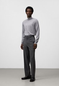 Maglione grigio a maniche lunghe e collo alto abbinato a pantaloni grigi dalle linee classiche. Il modello indossa mocassini neri, mostrando un aspetto pulito e strutturato.