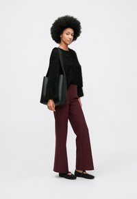 Fekete bolyhos pulóver, bordó trapéz nadrág, fekete tüskékkel díszített cipők és fekete válltáska. A modell egy semleges háttér előtt áll.