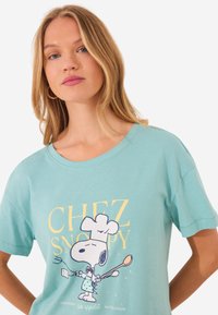 T-shirt verde menta a maniche corte con grafica di Snoopy cuoco con cucchiaio e utensili da cucina, materiale in cotone, vestibilità rilassata.