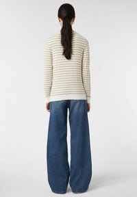 Gestreifter beiger und cremfarbener Pullover mit langen Ärmeln, kombiniert mit weiten blauen Jeans. Mit gerippten Bündchen und Saum.