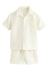 Cămașă crem cu mâneci scurte, nasturi și buzunar la piept, asortată cu pantaloni scurți cu același model, ambele având un design tricotat texturat.