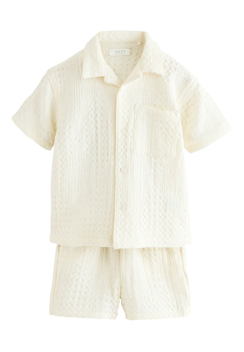 Cămașă crem cu mâneci scurte, nasturi și buzunar la piept, asortată cu pantaloni scurți cu același model, ambele având un design tricotat texturat.