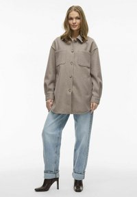 Overdimensioneret beige uld skjortejakke med to forlommer, knaplukning og optrukne ærmer, parret med afslappede lyse himmelblå jeans og hælede støvler.