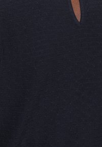 Marinblå stickad topp med en texturerad mönster, har en V-formad halsringning, mjukt tyg och en avslappnad passform.