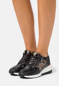 Black and metallic sneaker with textured fabric panels, lace and zip closure, a white sole, and logo detail on the tongue.