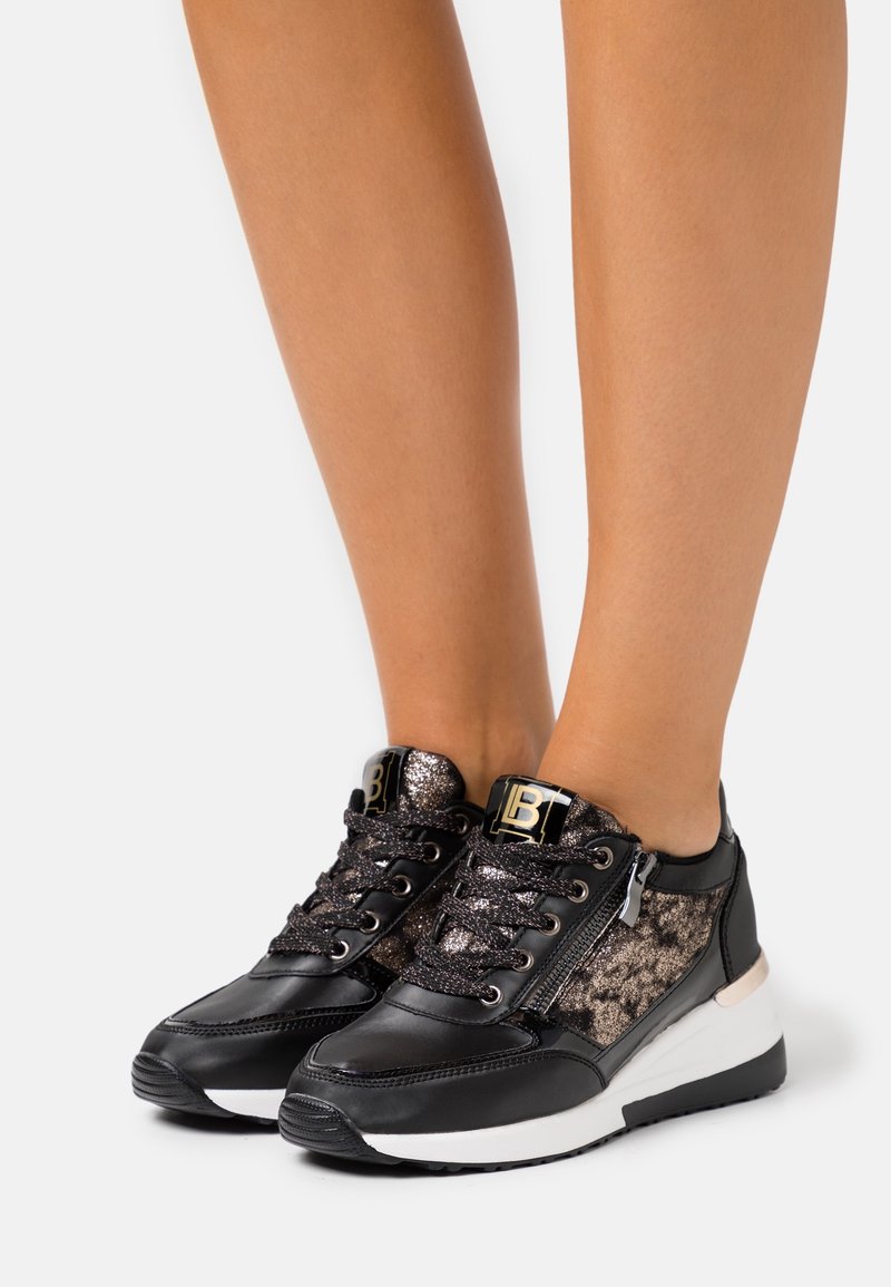 Black and metallic sneaker with textured fabric panels, lace and zip closure, a white sole, and logo detail on the tongue.