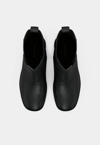 Un paio di stivali neri in pelle slip-on con punte arrotondate, con linguette sul retro, visti dall'alto su uno sfondo bianco.