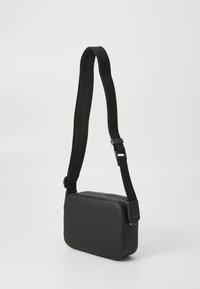 Black rectangular crossbody bag made of textured material, featuring a smooth zipper and an adjustable strap.