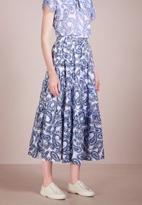 Jupe longue à imprimé cachemire floral en bleu et blanc, avec un design à volants et une ceinture élastique. Associée à des baskets blanches.