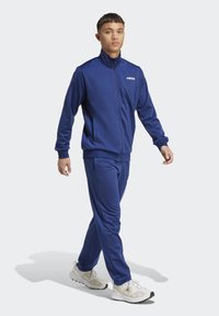 Kungslila träningsoverall i slät tyg, med en dragkedjeförsedd jacka och matchande byxor. Setet har sidofickor och ribbade muddar.