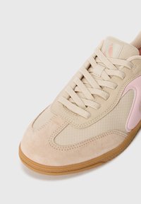 Valkoinen lenkkari vaaleanpunaisilla yksityiskohdilla, texturoitu verkko- ja sileä mokkamateriaali, litteät nauhat, pyöreä kärki ja kuminen pohja.