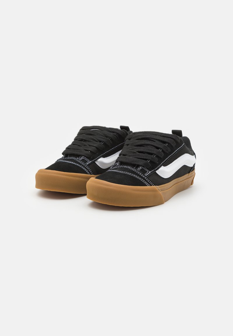 Sneaker in suede nero con dettagli a strisce bianche, lacci neri e suola in gomma color caramello, presentano un design a profilo basso e un colletto imbottito.