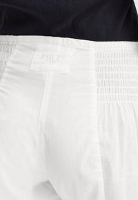 Vita byxor med en resårmidja och en etikett märkt "PULZ JEANS." Tyget verkar lätt och slätt med en subtil textur.