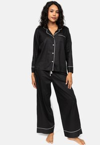 Conjunto de pijama de satén negro que incluye una camisa con botones, bolsillo en el pecho y ribete blanco, combinada con pantalones negros holgados.