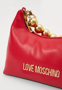 Red leather handbag with a rounded shape, gold beaded chain, and embossed "LOVE MOSCHINO" logo on the front. Smooth texture and shiny accents.