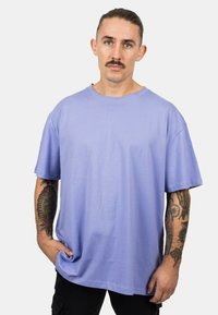 Light purple cotton t-shirt with short sleeves, round neck, and a loose fit. Features visible seam detailing and worn over black pants.